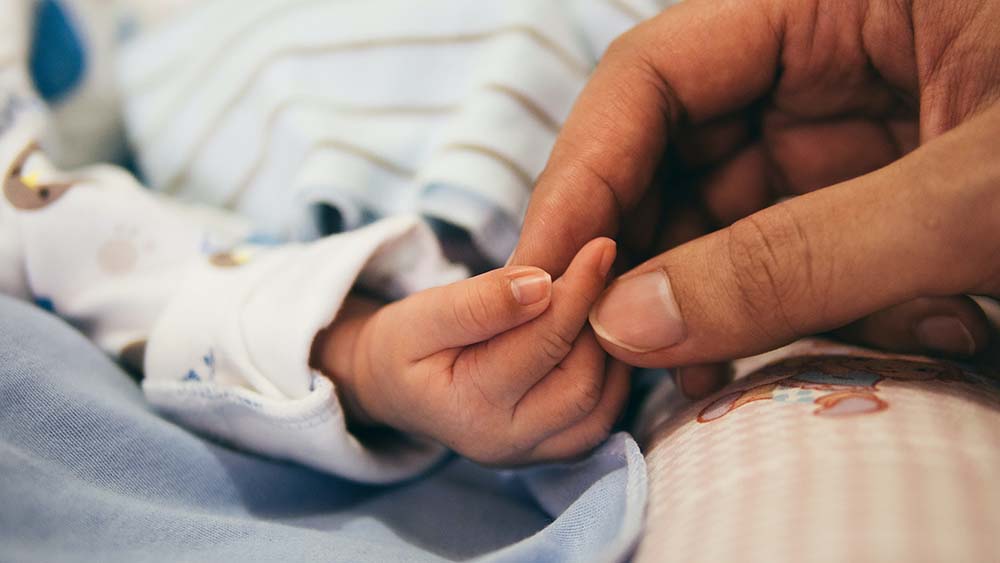 A female's hand holding a baby's hand on a light blue blanket
