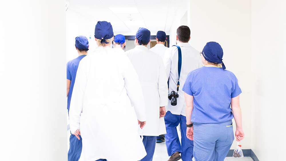Nurses and doctors walking away down a white corridor